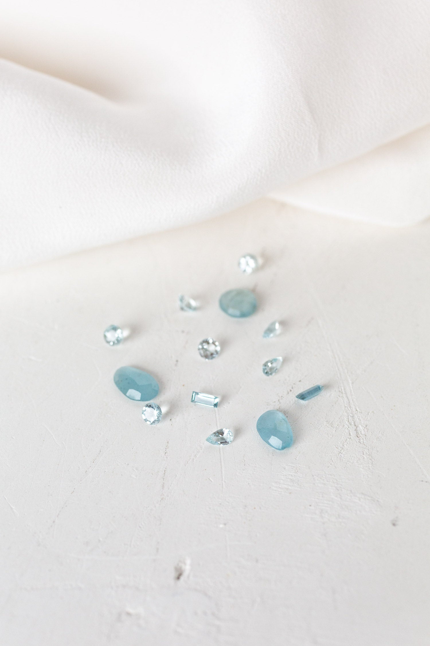 Blue Aquamarine stones on white cloth, perfect for March birthdays. Aquamarine birthstones symbolize serenity and clarity.
