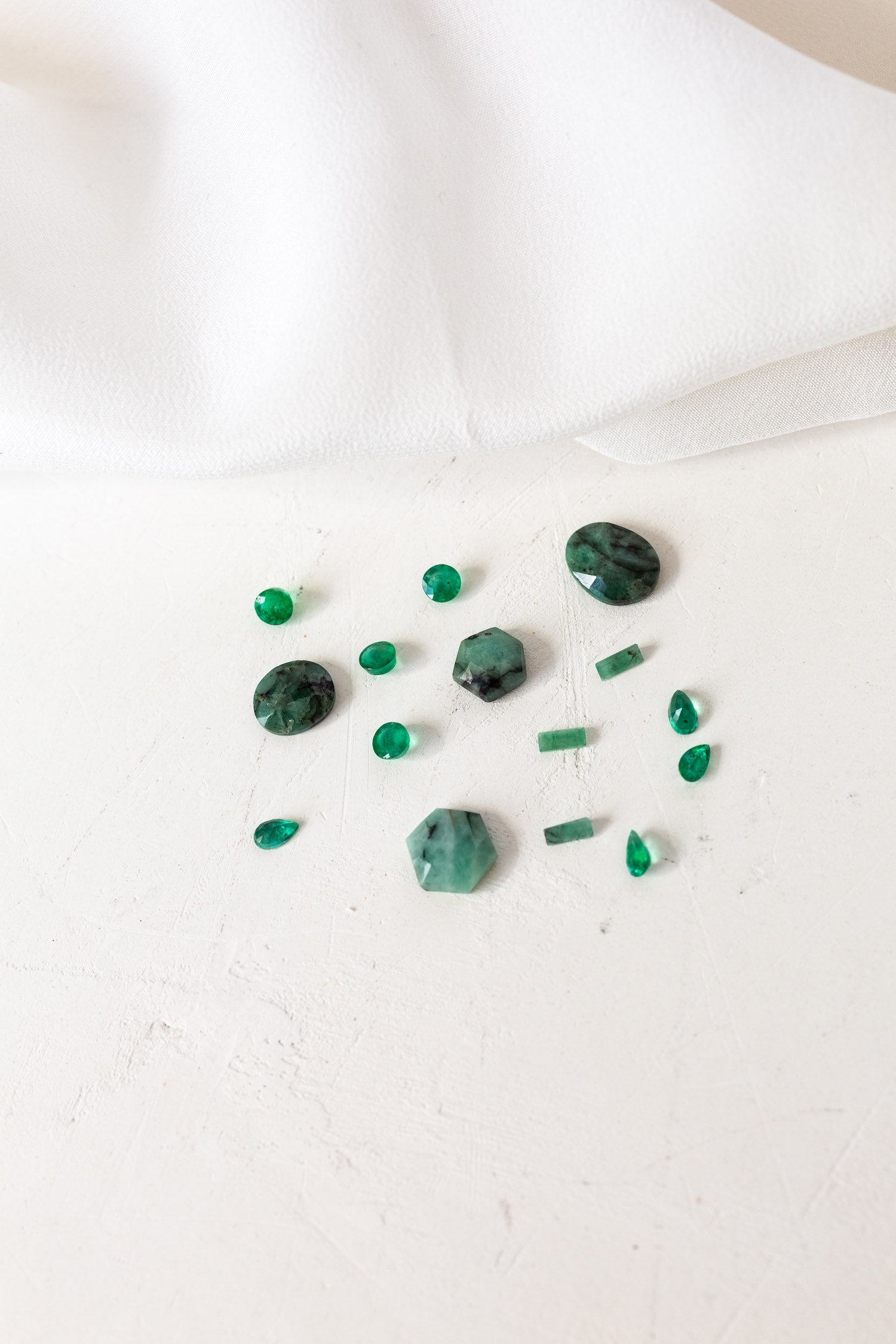 A collection of green emerald birthstones arranged on a white cloth.