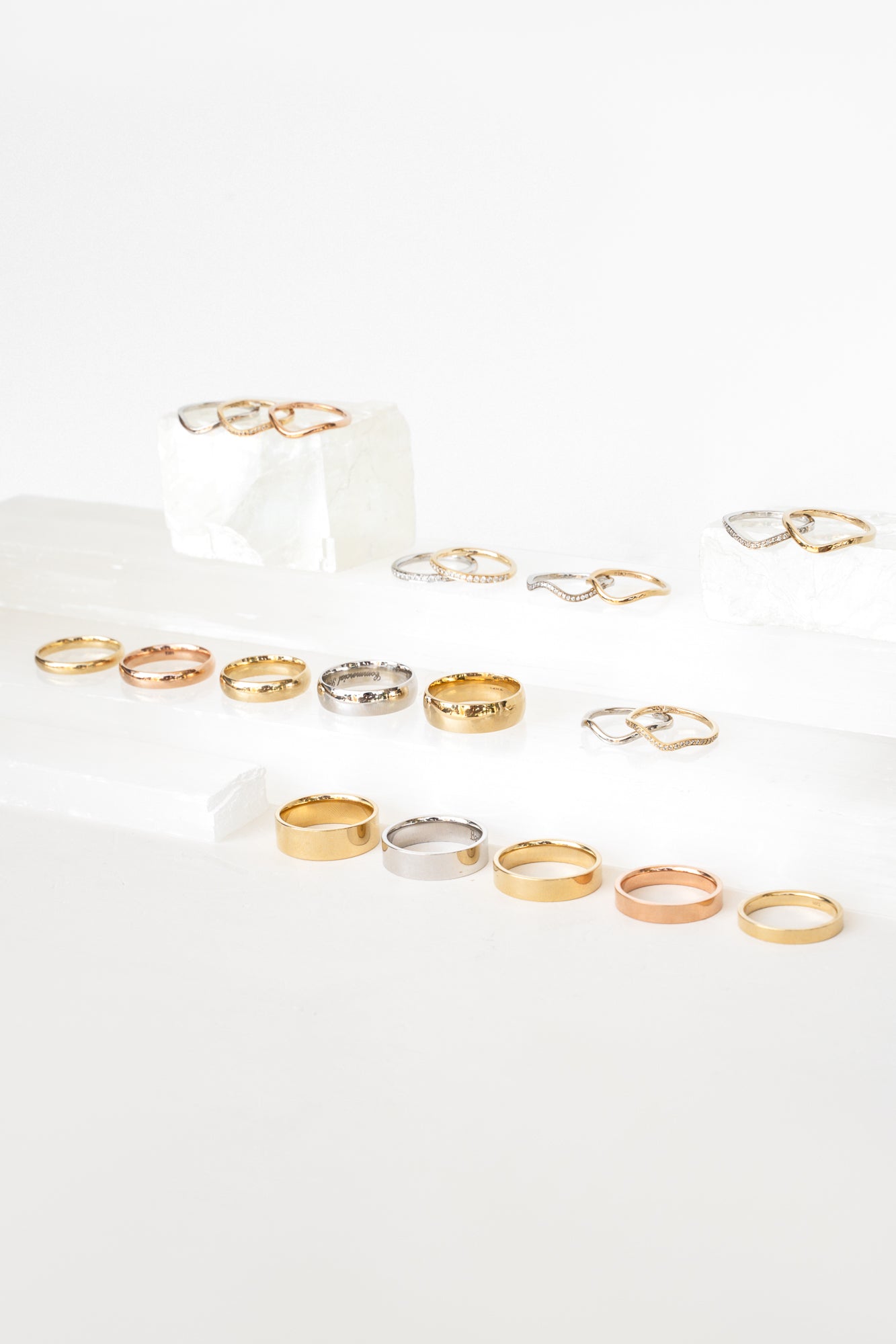 A variety of gold and silver wedding bands displayed on a white surface.