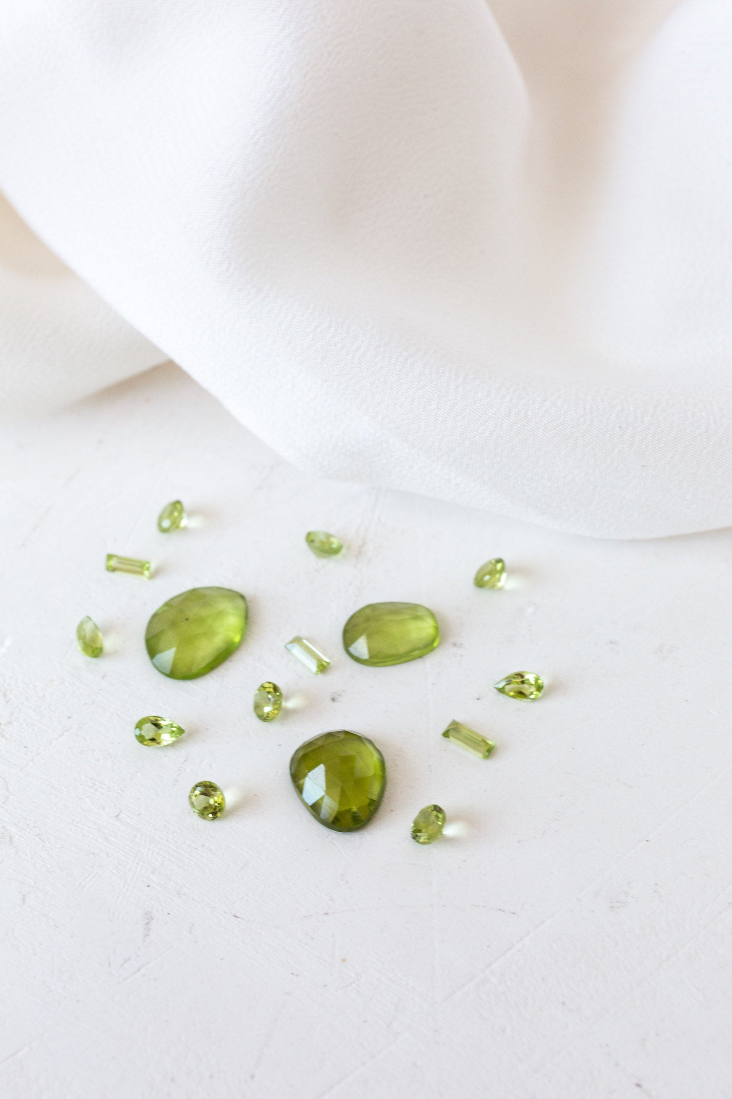 Green peridot stones on white cloth - birthstones for August, symbolizing strength and protection.