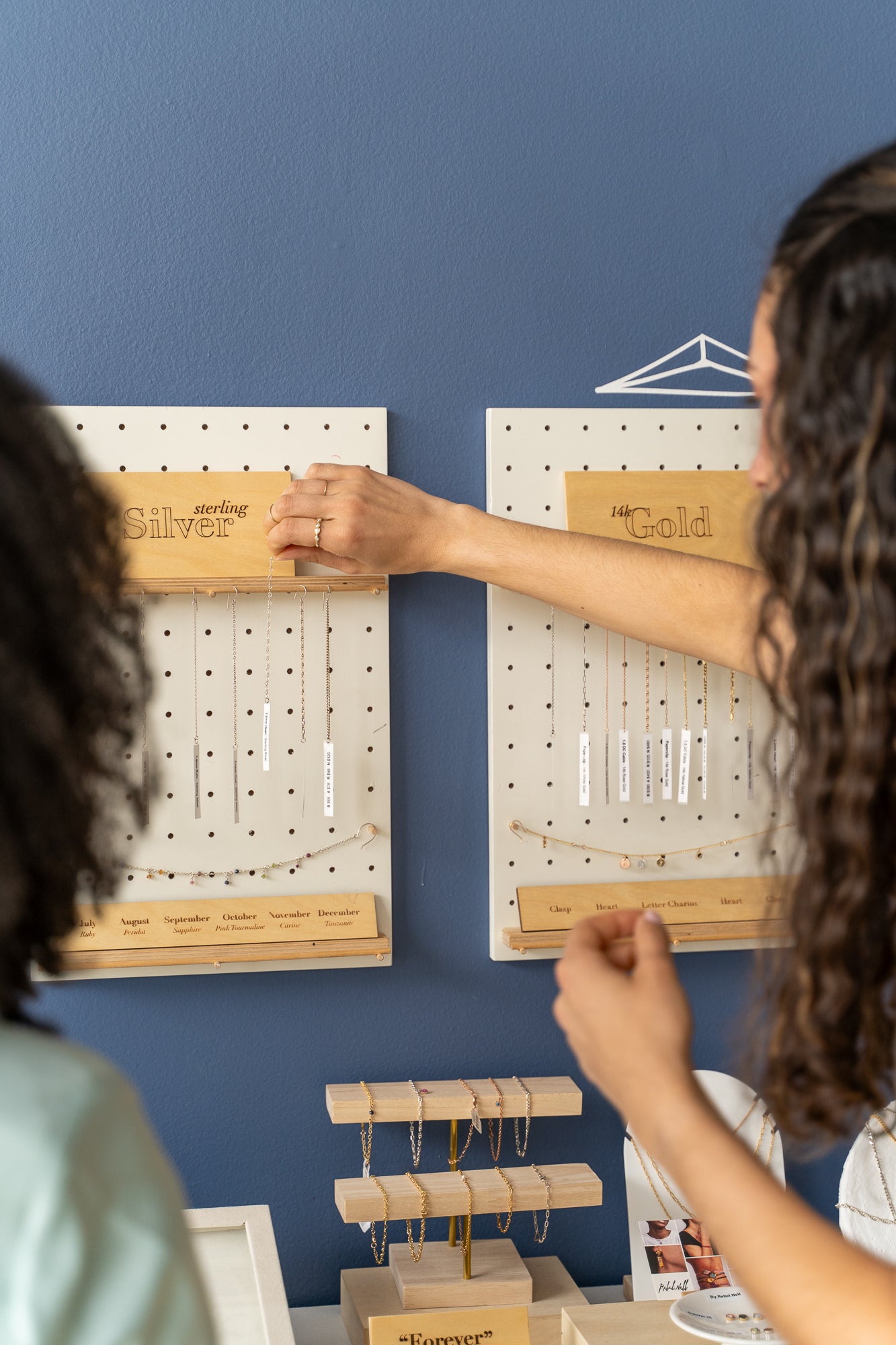 Two women examining a pegboard filled with various pieces of jewelry chains