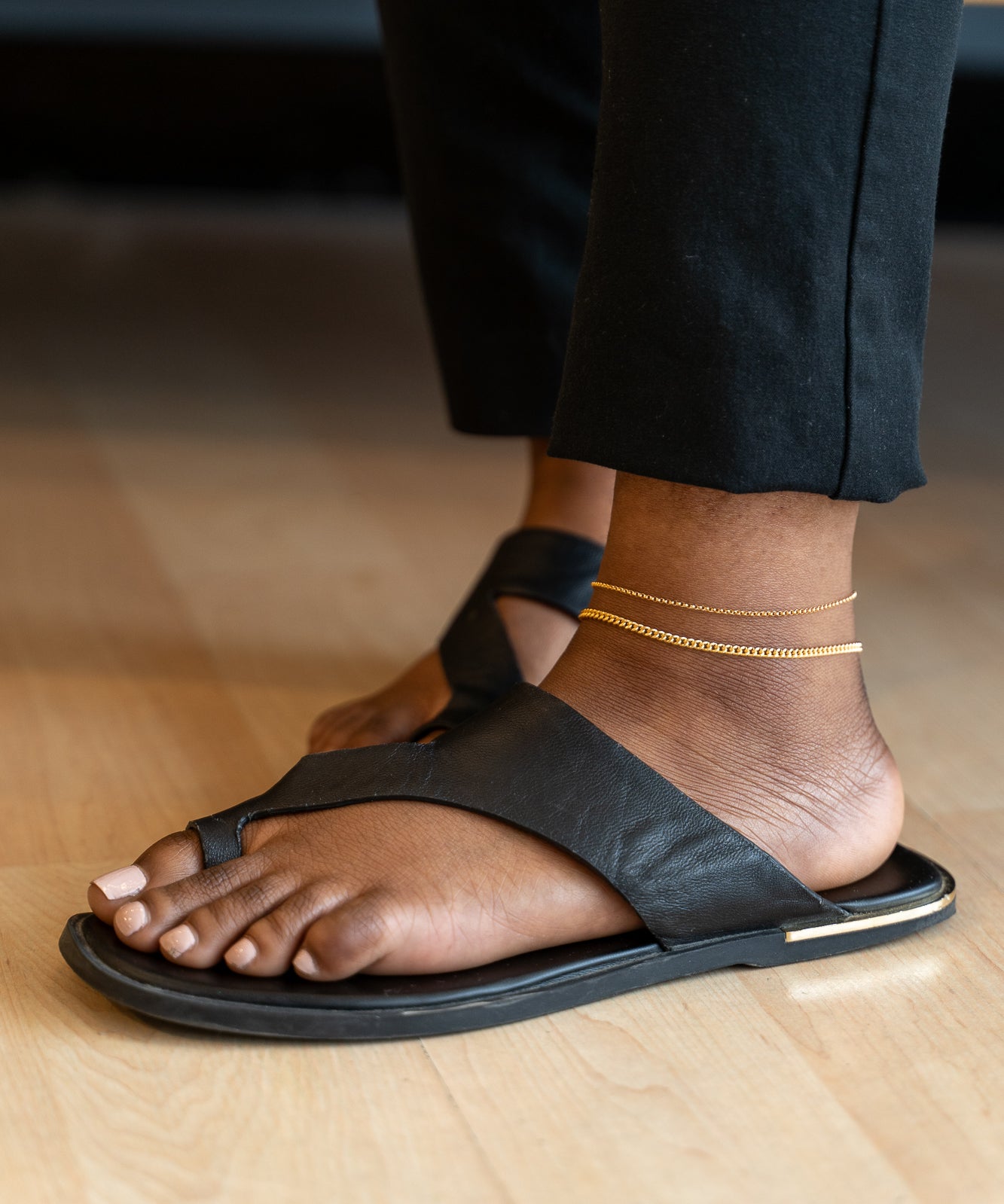 A woman wearing black sandals and gold chains, featuring a Forever Linked Anklet.