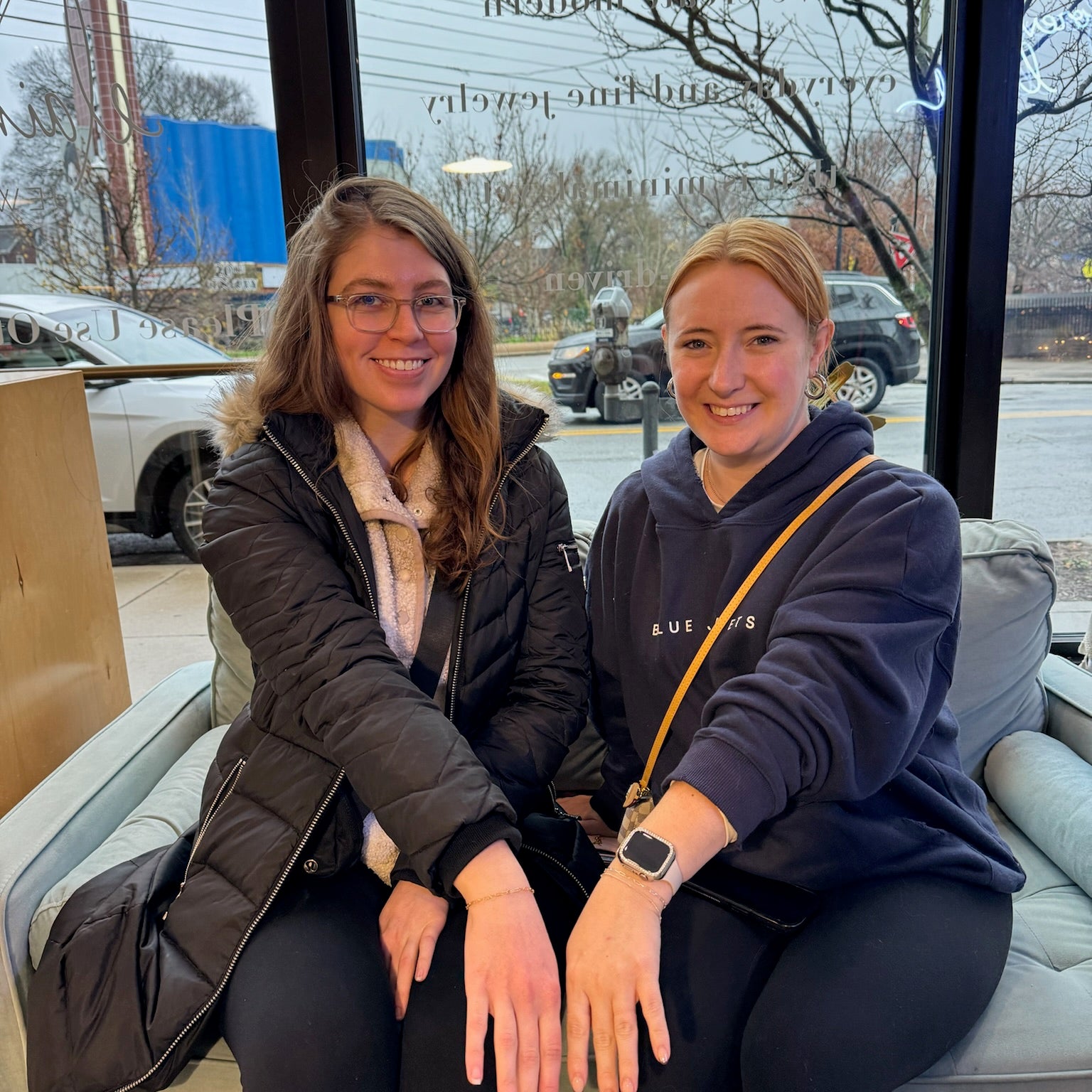 Two women sitting on a couch, leaning towards each other, with their hands gently resting on their knees