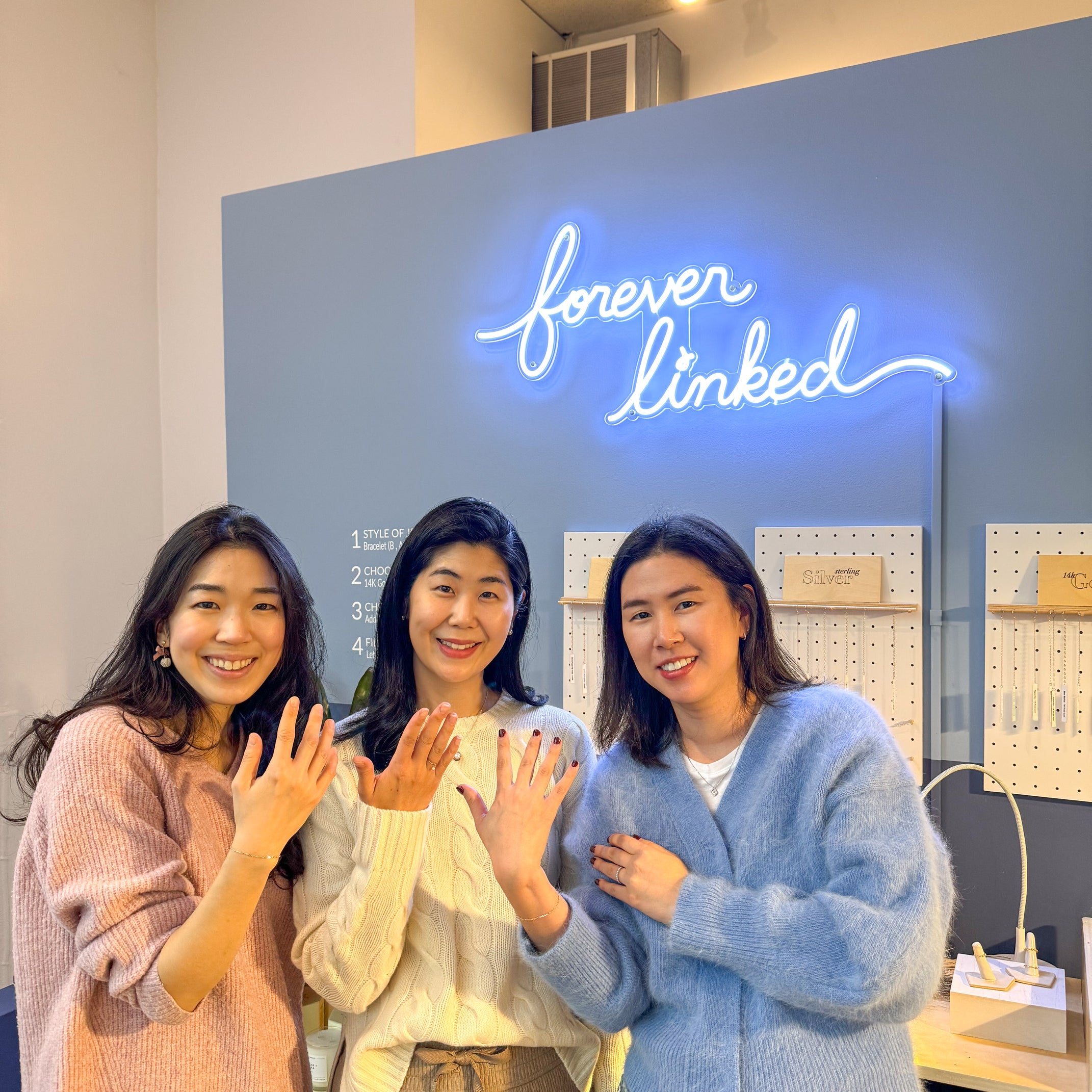 Three girls smiling in front of a sign that reads "forever linked".