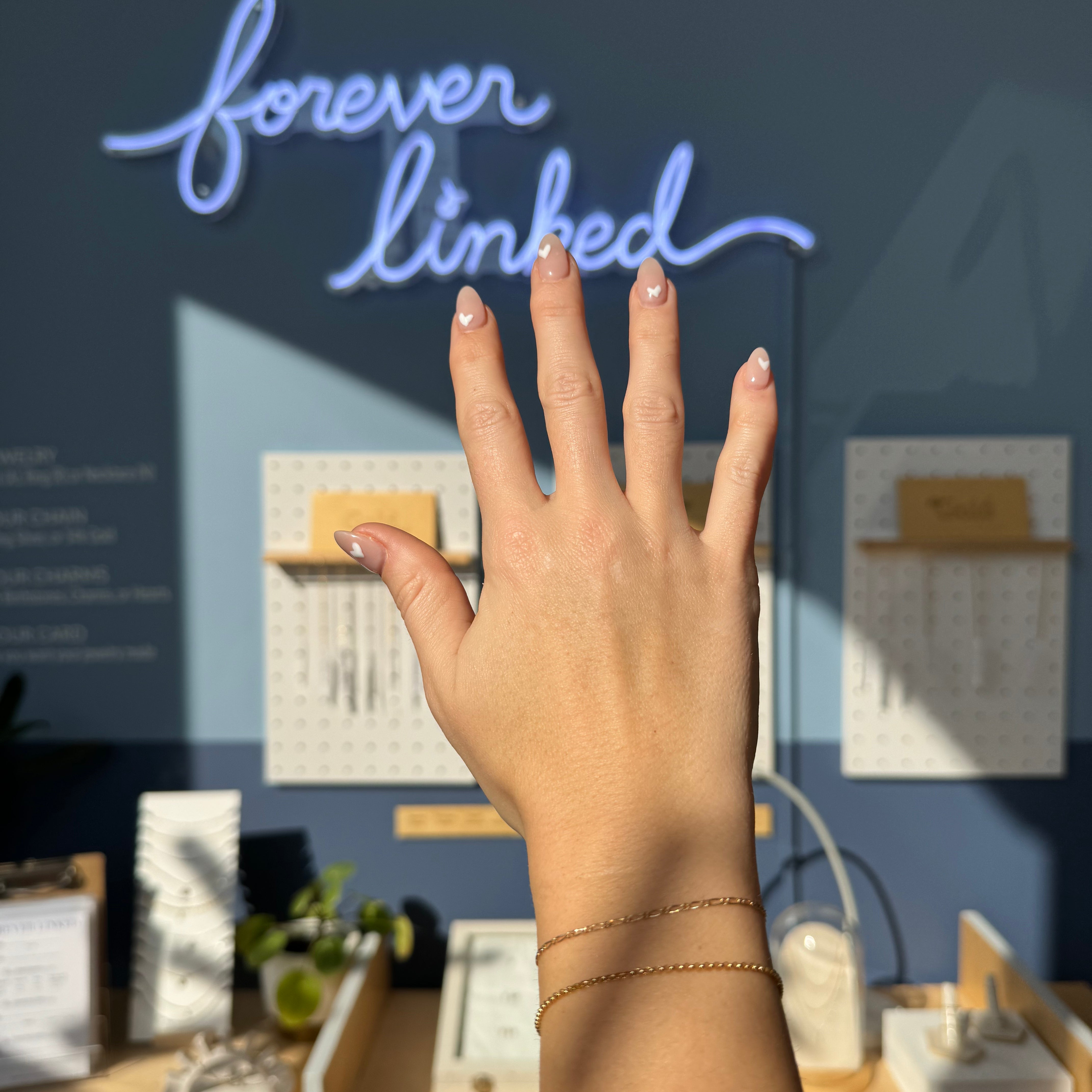A hand holds a bracelet with a neon sign that reads "forever linked", symbolizing a strong and everlasting connection.