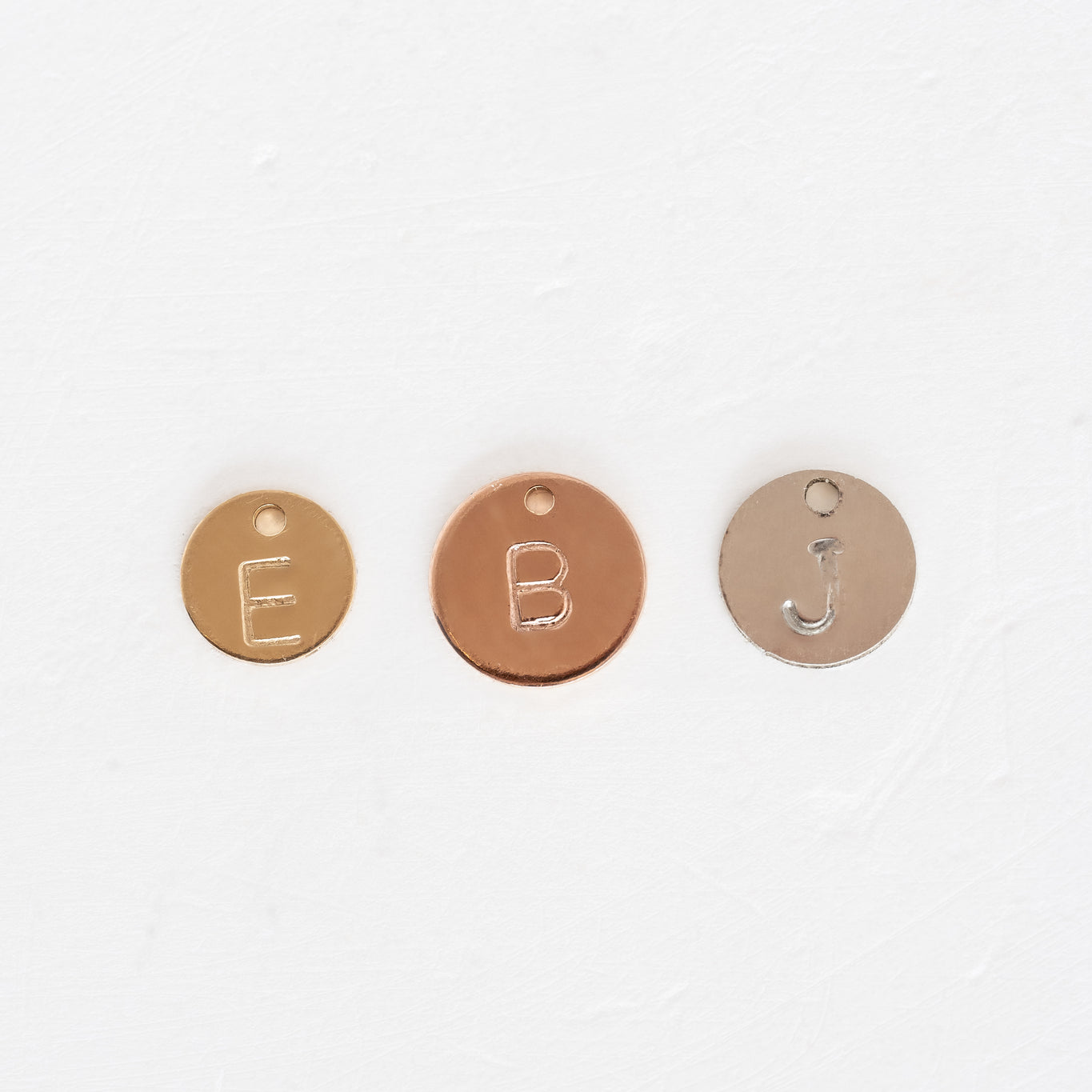 Three metal charms with stamped letters e, b, and j, representing Forever Linked Stamped Disks.