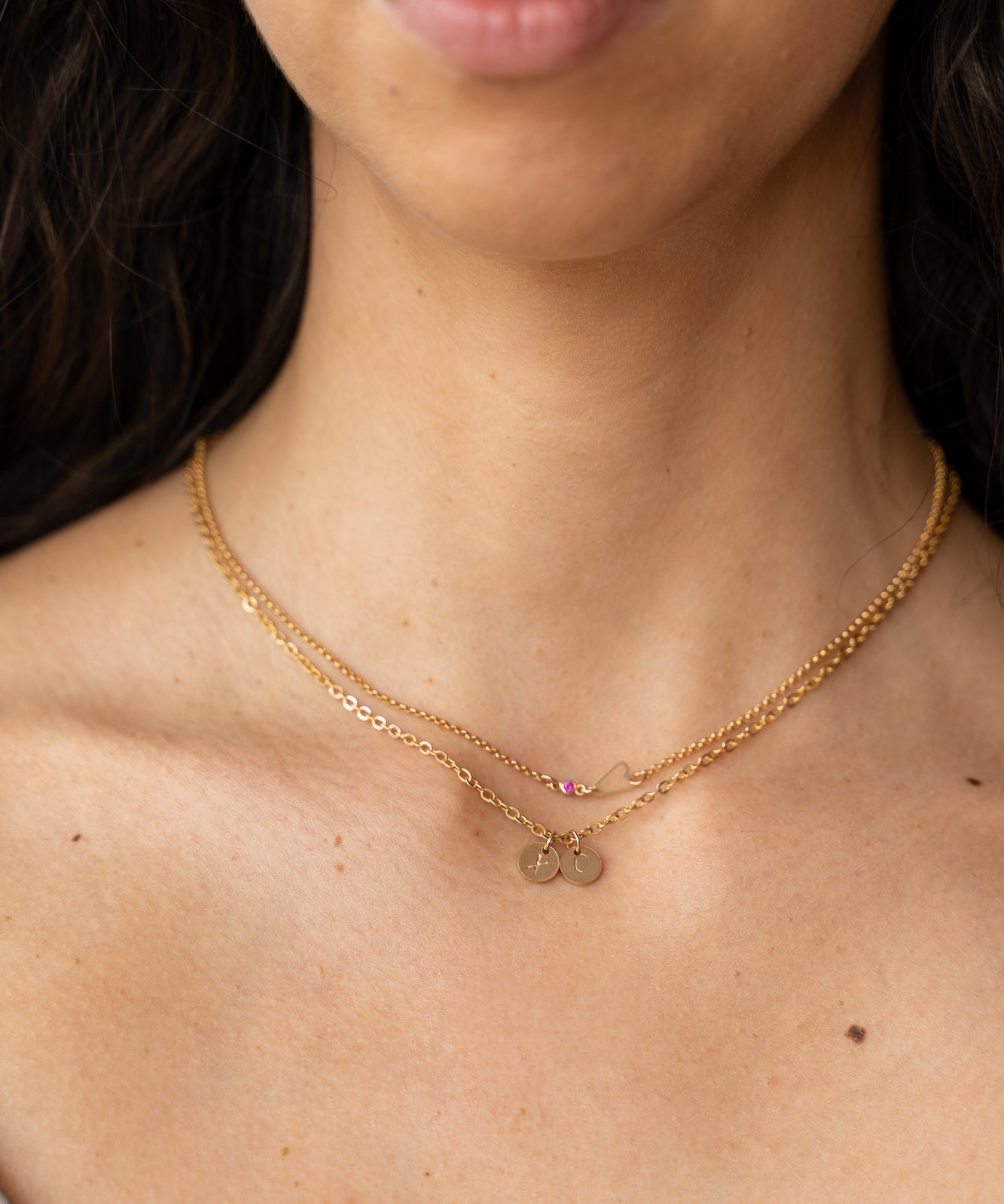 A woman wearing a gold necklace with a heart charm, symbolizing eternal connection and stamped charms