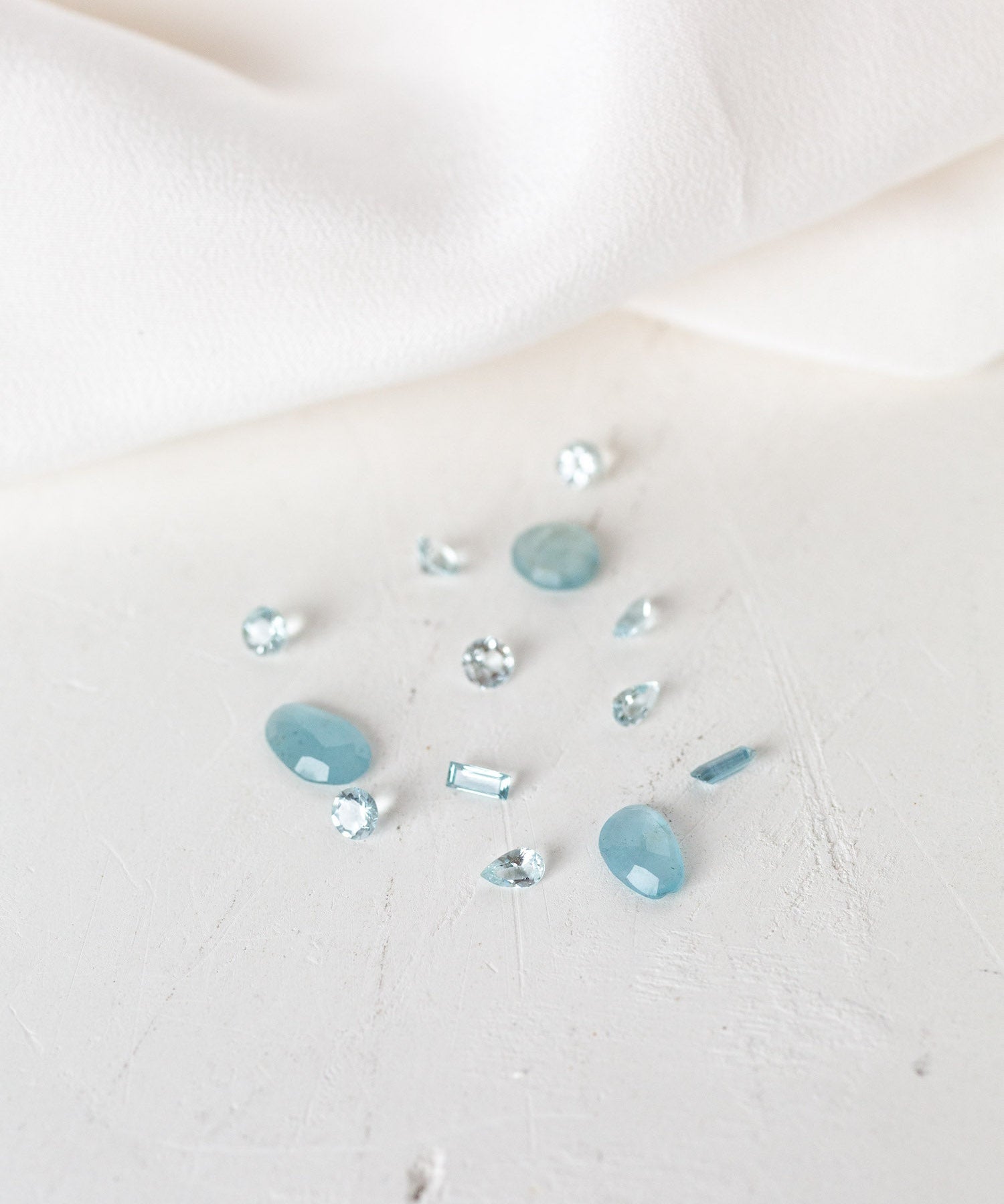 Blue Aquamarine stones on white cloth, perfect for March birthdays. Aquamarine birthstones symbolize serenity and clarity.