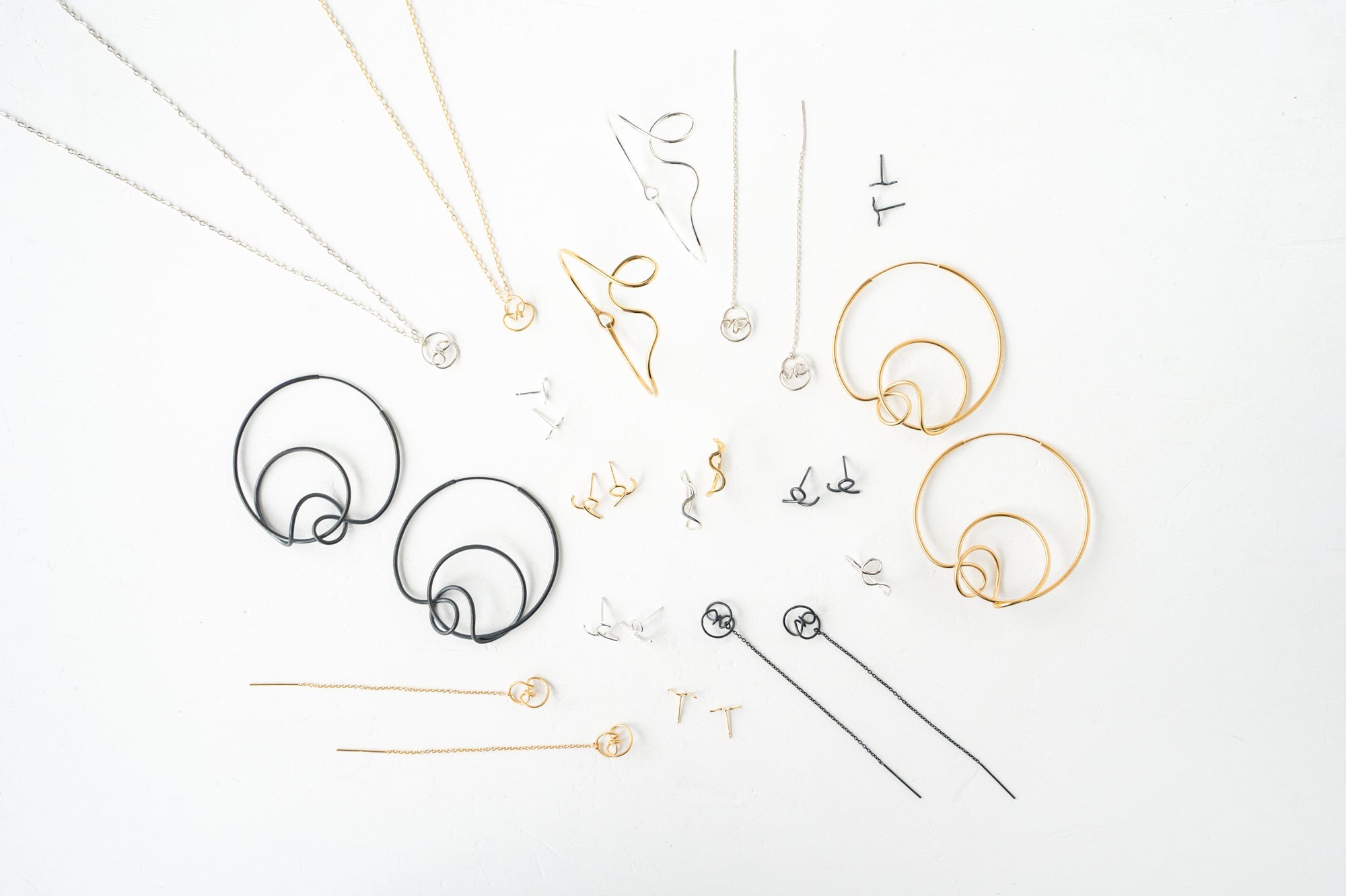 Various pieces of gold and silver jewelry are arranged on a white surface as part of the Calligraphy Collection, highlighting the beauty of pen strokes.