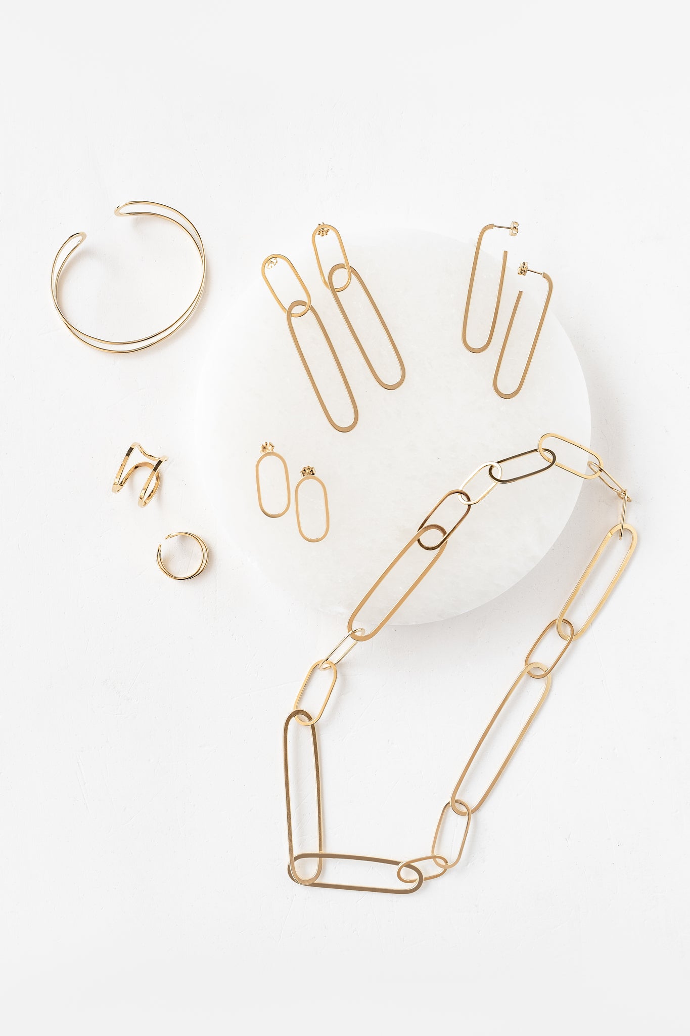 Gold chain necklace, earrings, and bracelet from the Ellipse collection with paperclip chain link design on a white surface.