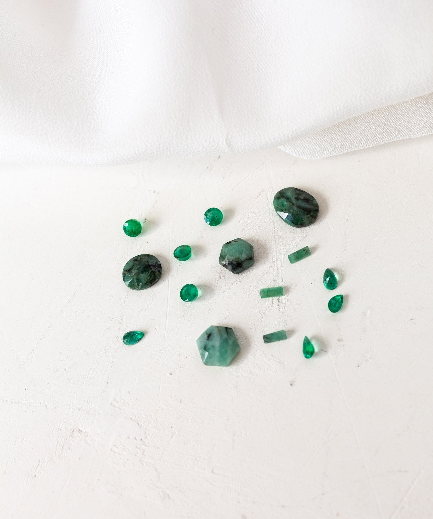 A collection of green emerald birthstones arranged on a white cloth.
