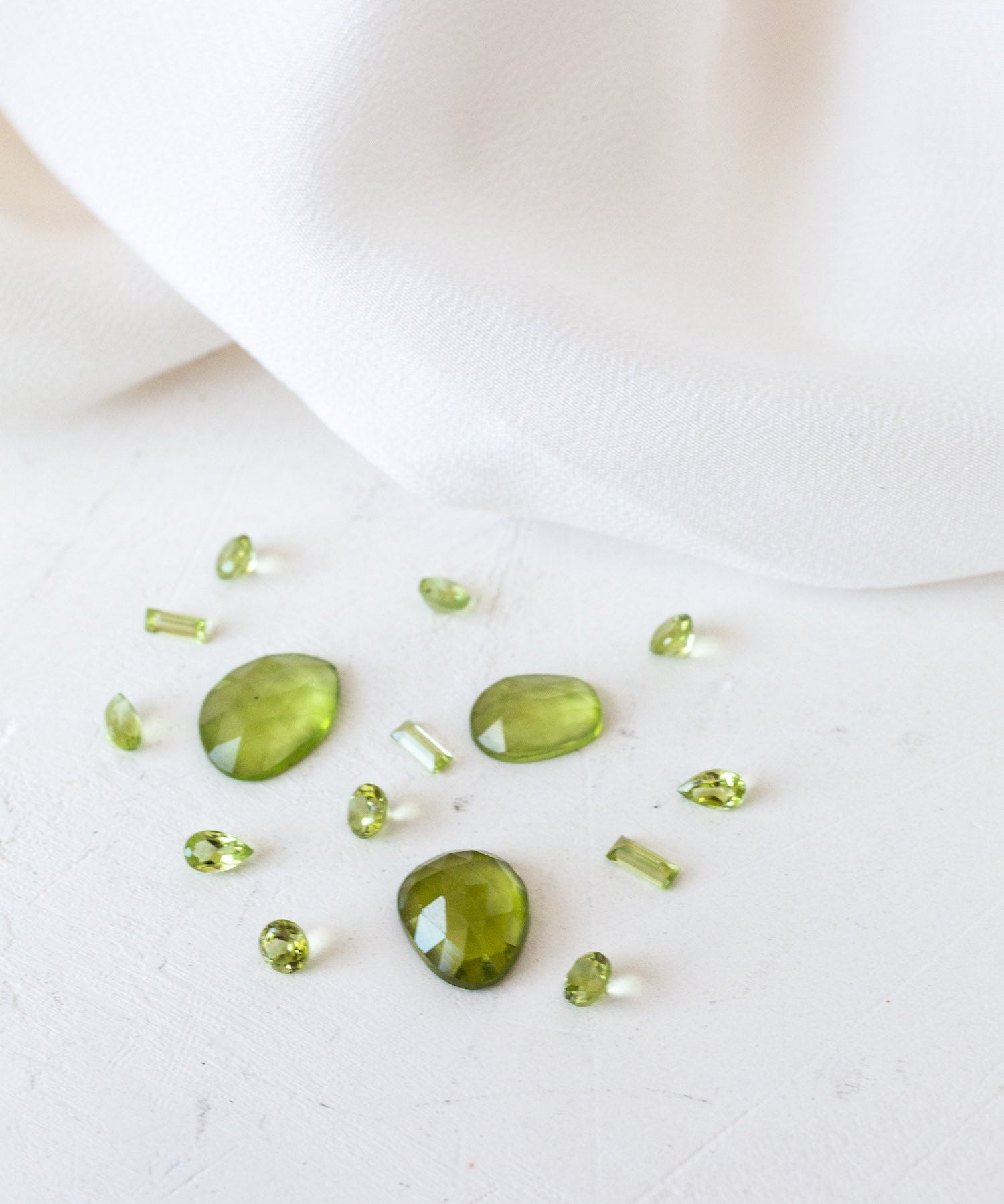 Green peridot stones on white cloth - birthstones for August, symbolizing strength and protection.