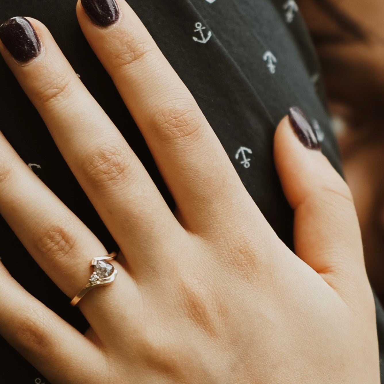 Close-up of a hand with a ring on a person wearing a black shirt with anchor patterns, with another person partially visible.