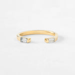 A gold open cuff ring featuring two rectangular clear baguette-cut gemstones on each end, photographed on a clean white background.
