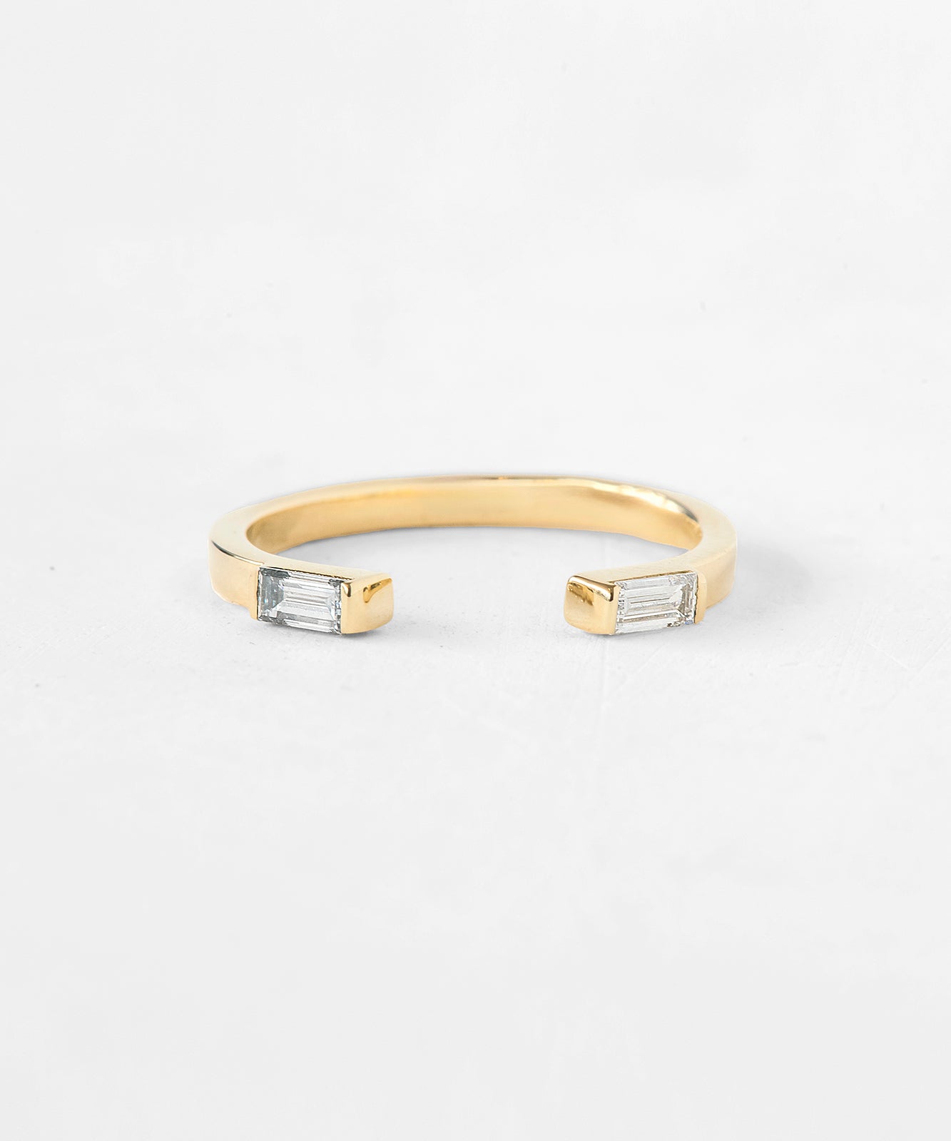 A gold open cuff ring featuring two rectangular clear baguette-cut gemstones on each end, photographed on a clean white background.