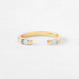 A gold open cuff ring featuring two rectangular clear baguette-cut gemstones on each end, photographed on a clean white background.
