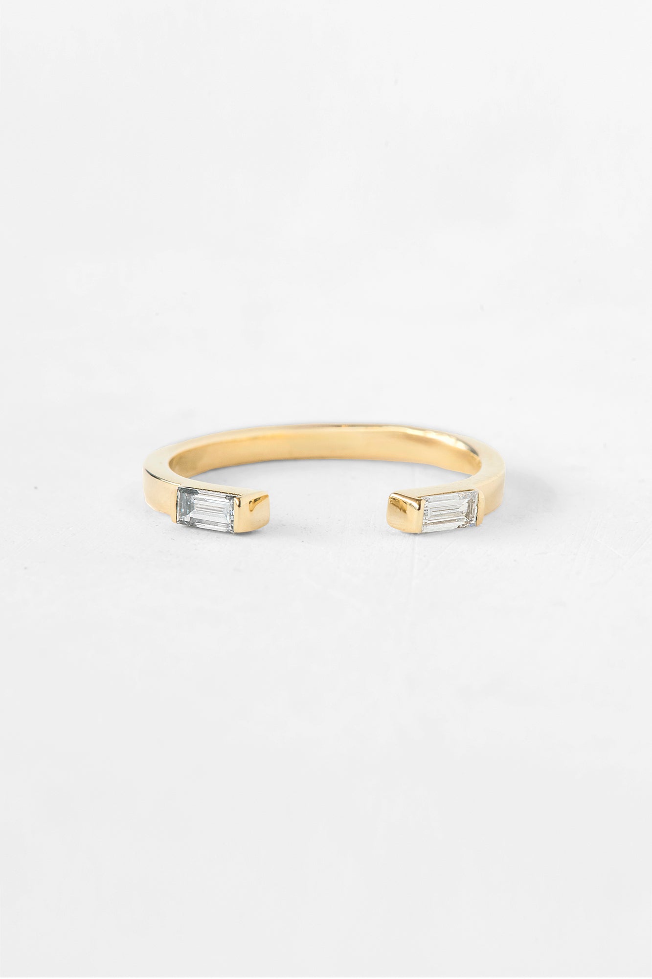 A gold open cuff ring featuring two rectangular clear baguette-cut gemstones on each end, photographed on a clean white background.