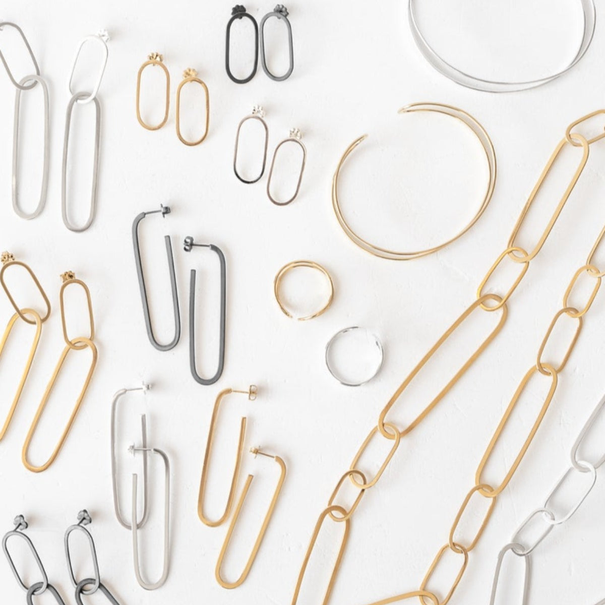 A variety of oblong silver and gold jewelry pieces displayed together, including necklaces, bracelets, and rings