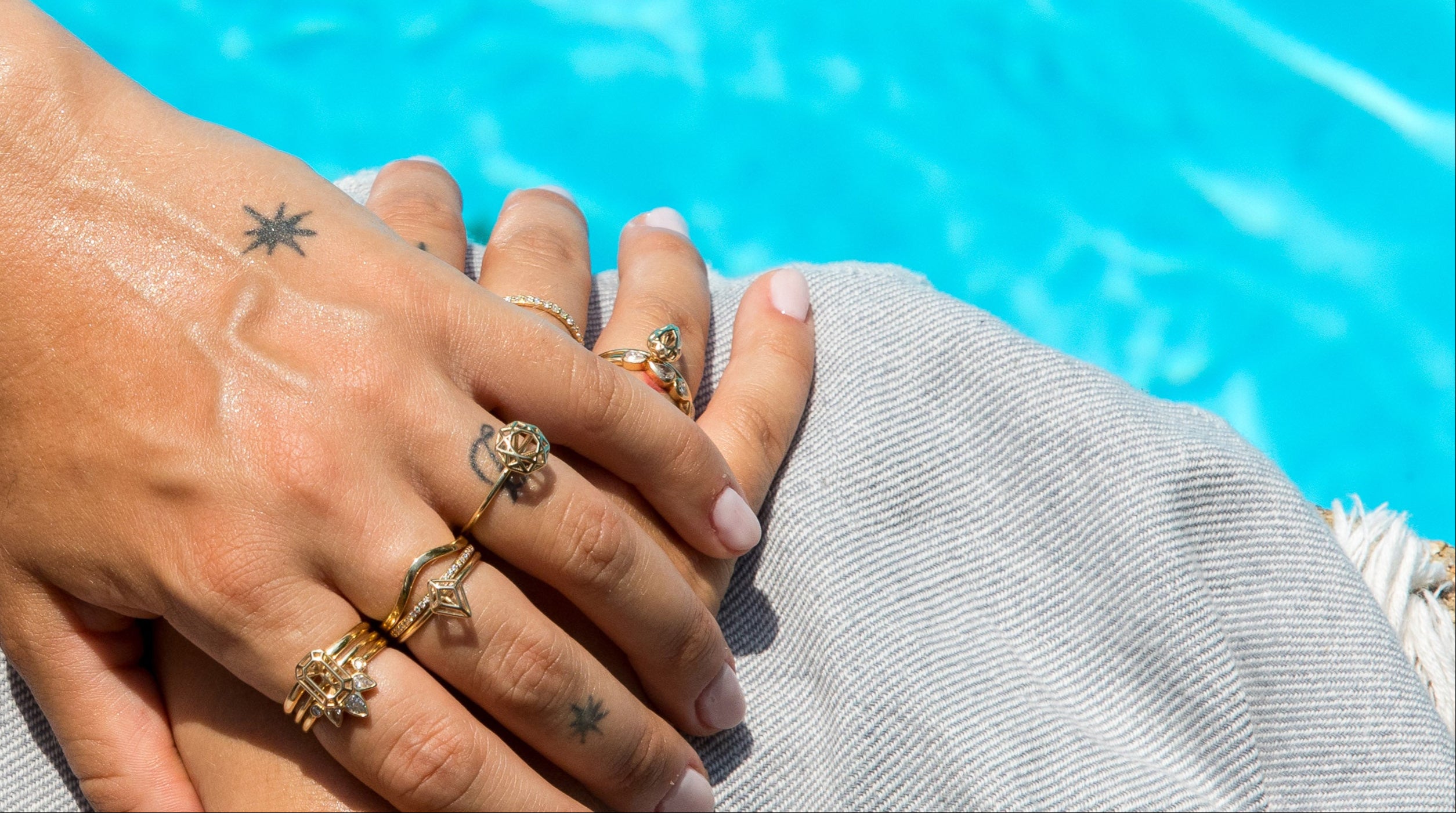 Multiple Gemma Rings by Elaine B Jewelry being worn by woman on a blanket next to a bright blue pool. 