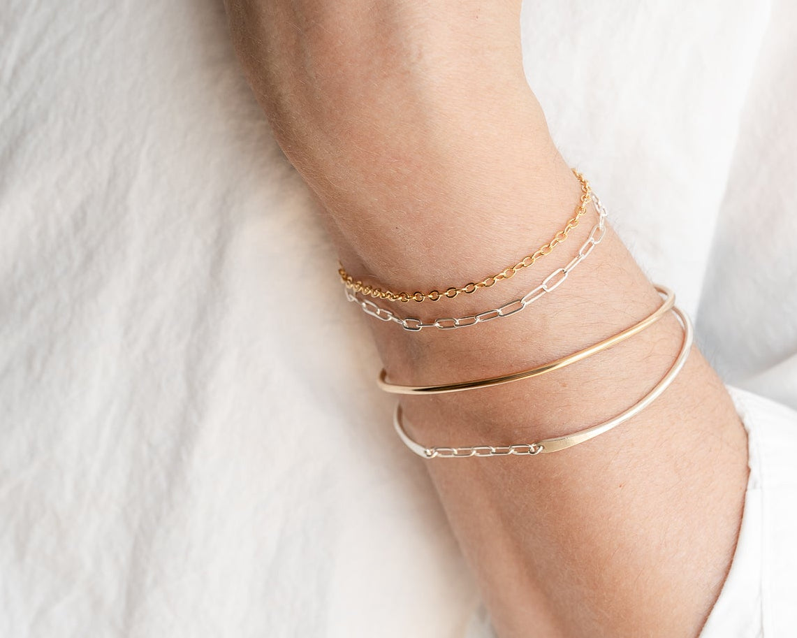 Permanent jewelry on a person's wrist with gold bracelets on a white background
