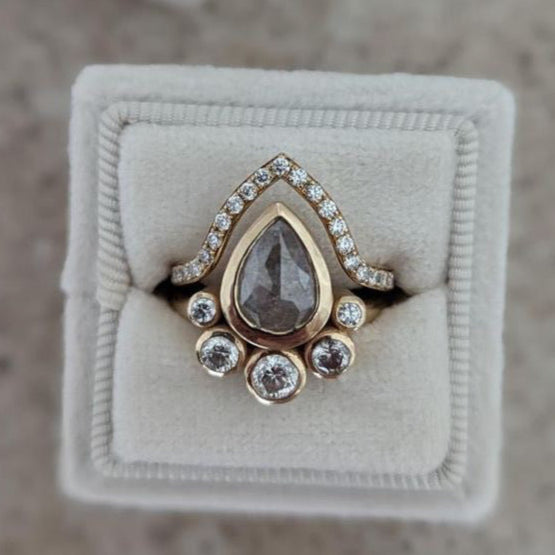 Gold ring with a teardrop-shaped gemstone on a beige velvet cushion