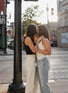 Two women embracing on a city street corner with buildings and traffic lights in the background.